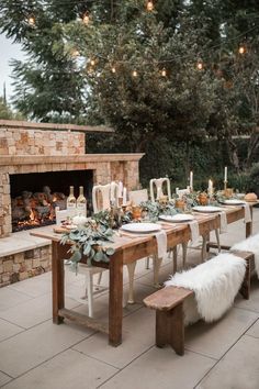 an outdoor dining table set up with candles, greenery and white fur rugs