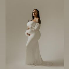 a pregnant woman in a white gown posing for the camera with her hands on her stomach