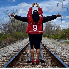 a man and woman standing on train tracks with their arms in the air, facing each other