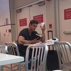 a man sitting at a table reading a book and holding a coffee cup in his hand