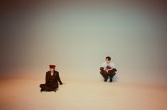 two men sitting on the ground in front of a white background