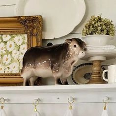 a cow figurine sitting on top of a shelf next to dishes and cups