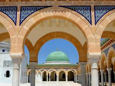 an archway leading to a building with a green dome on top and blue tiles around it