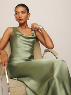 a woman in a green dress sitting on a chair holding a knife and looking at the camera