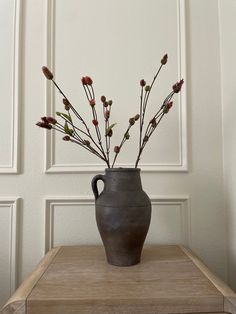 a vase filled with flowers sitting on top of a wooden table next to a white wall