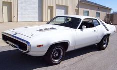 a white muscle car parked in front of a garage