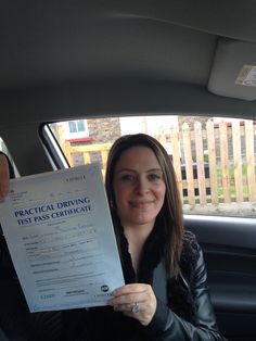 a woman sitting in the back seat of a car holding up a driving certificate