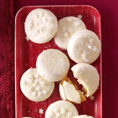 a red plate topped with white cookies covered in powdered sugar and sitting on top of a red table cloth