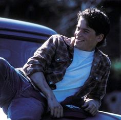 a young man sitting on the hood of a blue car with his feet propped up