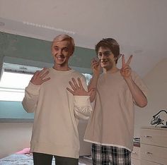 two young men standing next to each other with their hands in the air while making peace signs