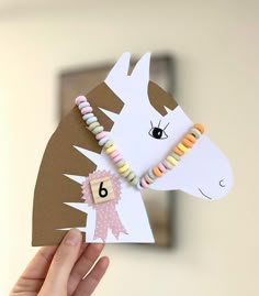 a hand holding up a paper horse with beads on it's head and number six