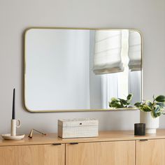 a wooden dresser topped with a mirror next to a plant