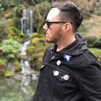 a man in black jacket and sunglasses standing next to a river with waterfall behind him