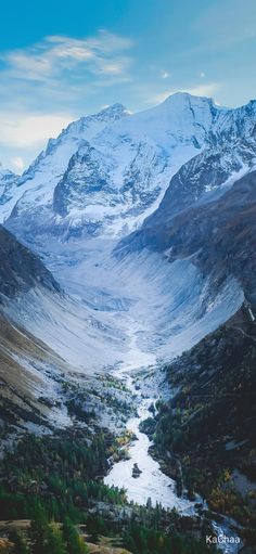 the mountains are covered in snow and green trees, with a river running between them