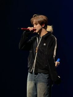 a young man standing on top of a stage holding a microphone in his hand and wearing a black jacket