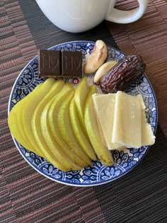 a blue and white plate topped with sliced apples and cheese next to a coffee cup