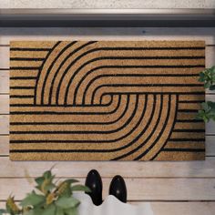 a pair of black shoes standing in front of a door mat that has a spiral design on it