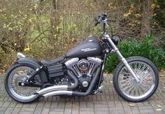 a black motorcycle parked on top of a brick road next to bushes and trees in the background