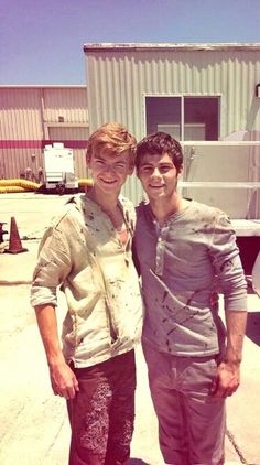 two young men standing next to each other in front of a building with a trailer behind them