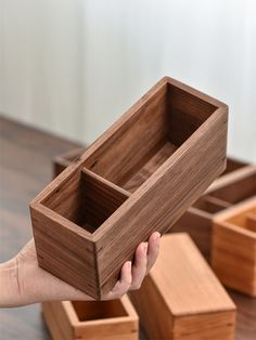 a person holding a wooden box in their left hand and several other wood boxes on the floor