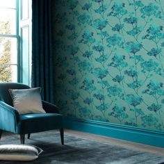 a blue chair sitting in front of a window next to a wall with flowers on it