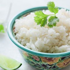 a bowl filled with rice and cilantro on top of a white table next to lime wedges