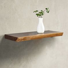 a white vase sitting on top of a wooden shelf next to a wall with a plant in it