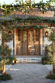 an entrance to a house with two wooden doors and some plants on the side walk