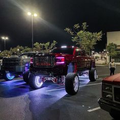 two pickup trucks parked in a parking lot at night with people standing around the cars