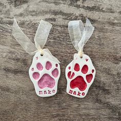 two handmade ceramic ornaments with red and white paw prints on them, one has the words make me