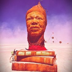 a large wooden statue sitting on top of a pile of luggage in the middle of a desert