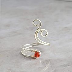 a silver wire ring with an orange bead sits on top of a marble surface