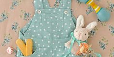 a stuffed rabbit sitting next to a blue polka dot overalls