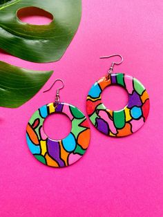 a pair of colorful earrings sitting on top of a pink table next to a plant