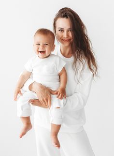 a woman holding a baby in her arms and smiling at the camera while wearing white