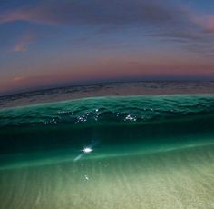 an ocean wave is seen from the water's surface at night, with stars in the sky