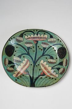 a decorative plate with flowers and leaves painted on the side, sitting on a white surface