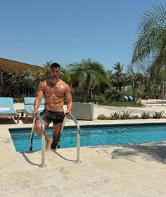 a man standing next to a swimming pool with no shirt on and his legs in the air