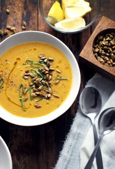 there is a bowl of soup on the table with spoons and lemon wedges