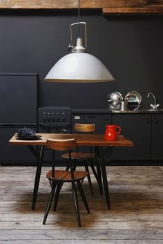 an industrial style kitchen with black walls and wooden flooring, white pendant light over the table