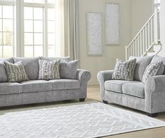 two gray couches sitting next to each other in front of a white stair case