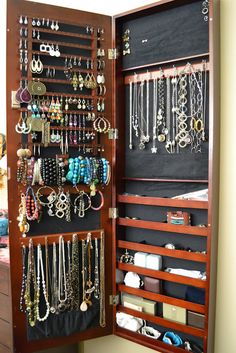 an open wooden jewelry cabinet filled with lots of necklaces