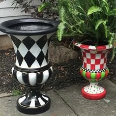 two vases sitting on the ground next to each other near some plants and flowers