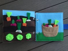 an open book with felt carrots and radishes in it on a wooden table