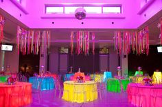 a room filled with lots of tables covered in neon colored cloths and streamers