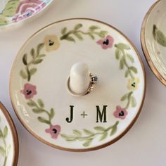 two wedding rings are placed in the middle of a floral ring dish with initials on it