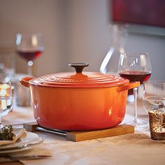 a table set with wine glasses and an orange casserole dish on top of it