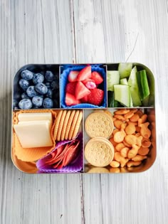 a bento box filled with fruit, crackers and cheese on top of a wooden table