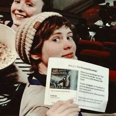 two women sitting in the stands at a baseball game, one holding up a card