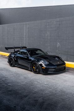 a black sports car parked in front of a gray brick wall with yellow rims